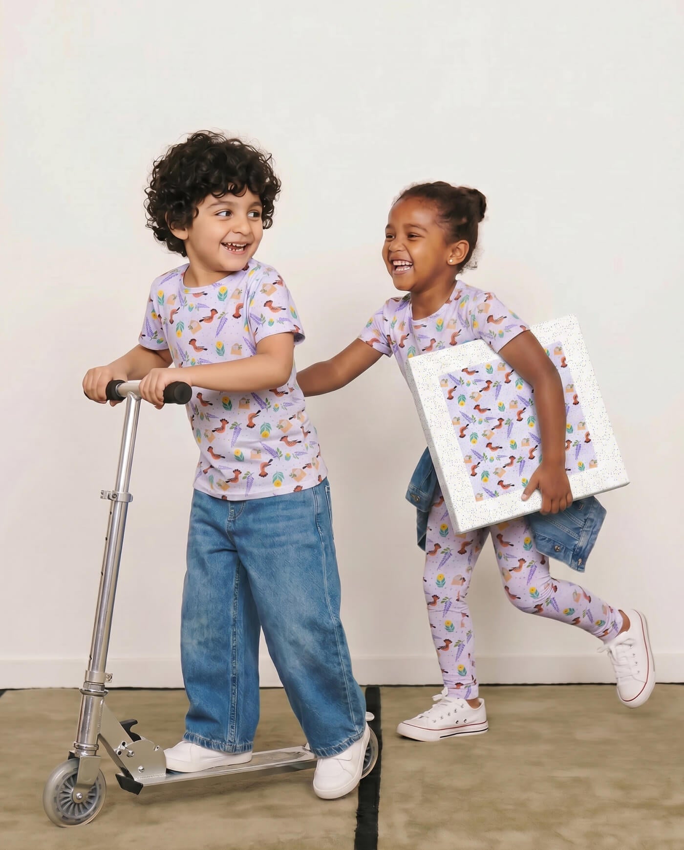 Children wearing matching lilac patterned wearable art pieces inspired by Islamic heritage, with one child carrying coordinating canvas wall art.