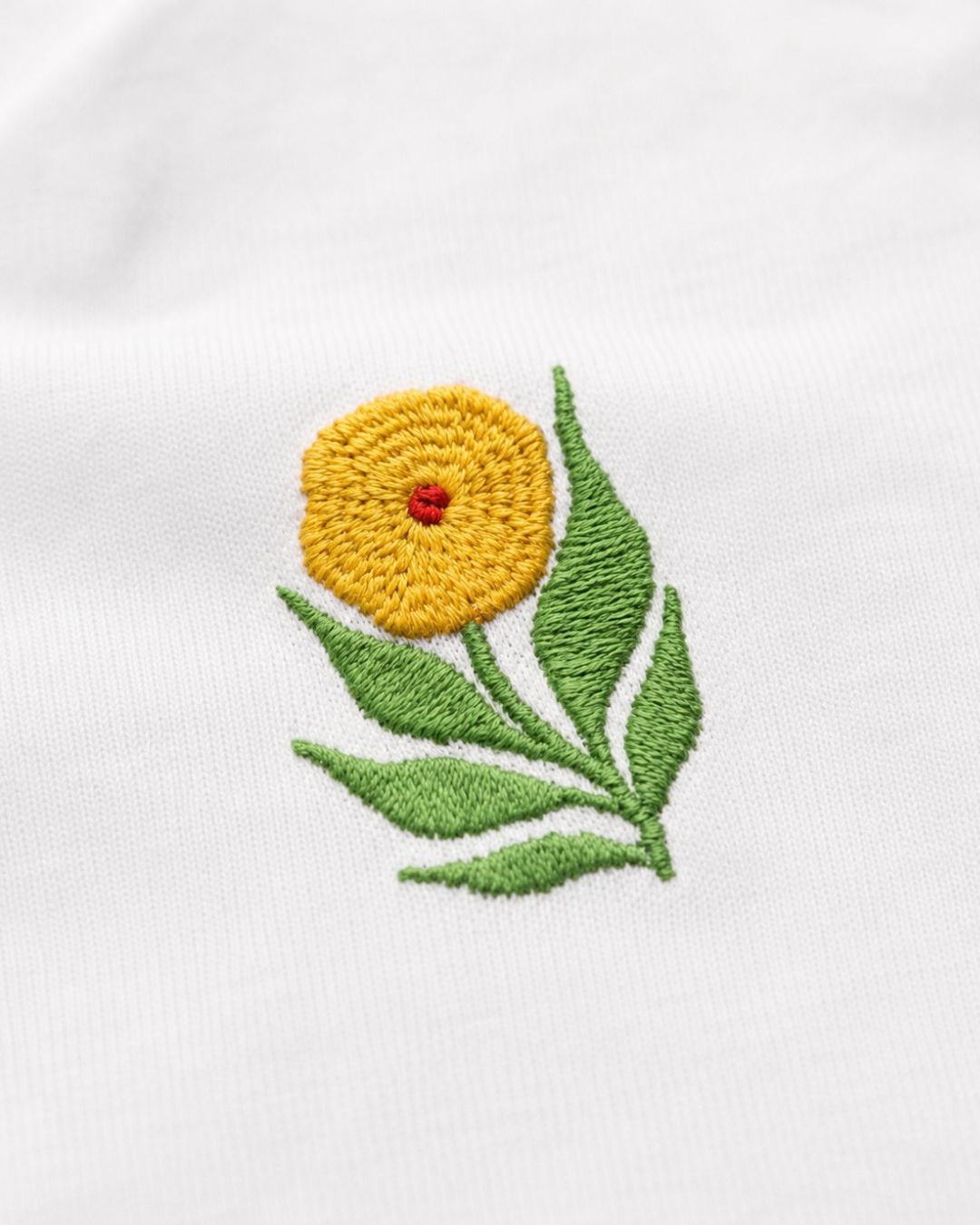 Embroidered yellow flower with green leaves on a white fabric background