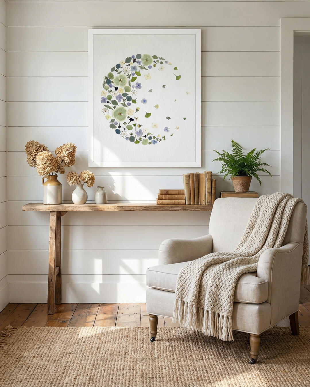 Fading moon dried flower art in a white frame, displayed on a wall above a wooden console in a calm, neutral living space.