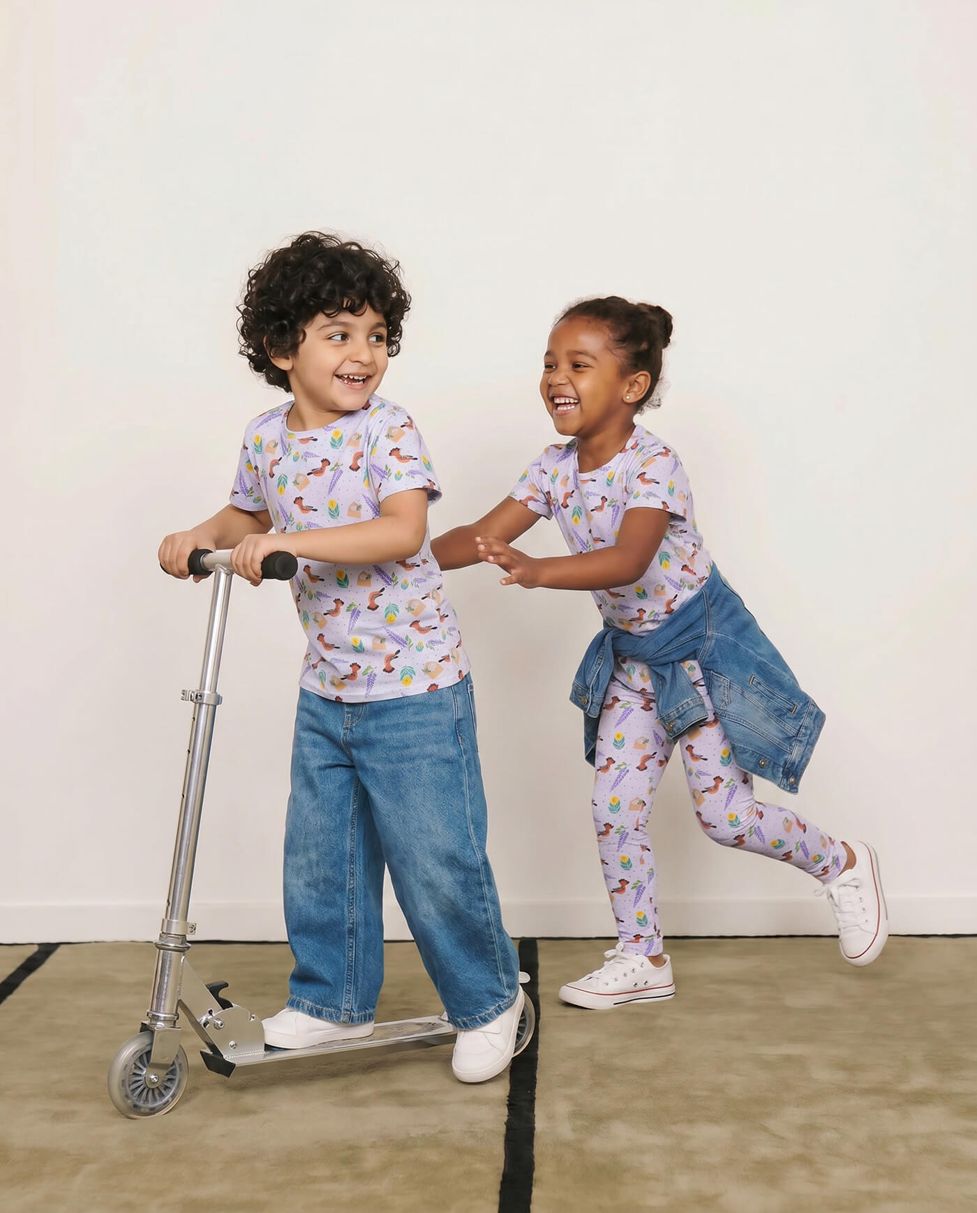 Two children wearing hoopoe bird kids t-shirts while playing indoors with a scooter.