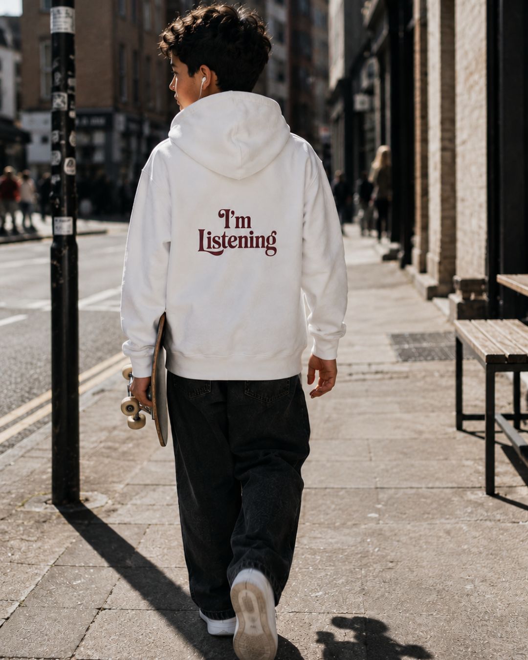 kids hoodie with “I’m Listening” back print worn by boy holding skateboard in city streetwear style