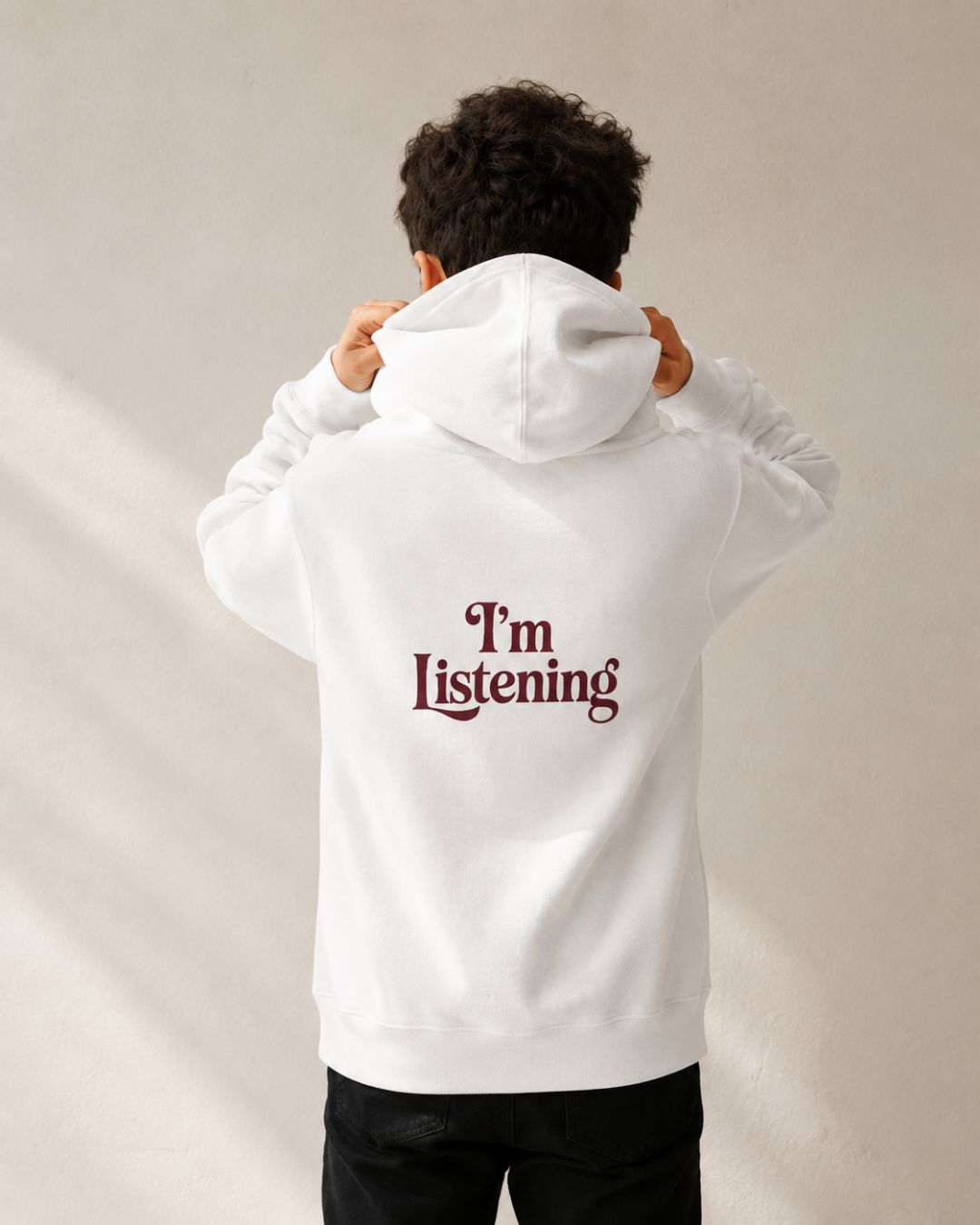 A young boy wearing a white hoodie with 'I'm Listening' text on the back against a neutral background