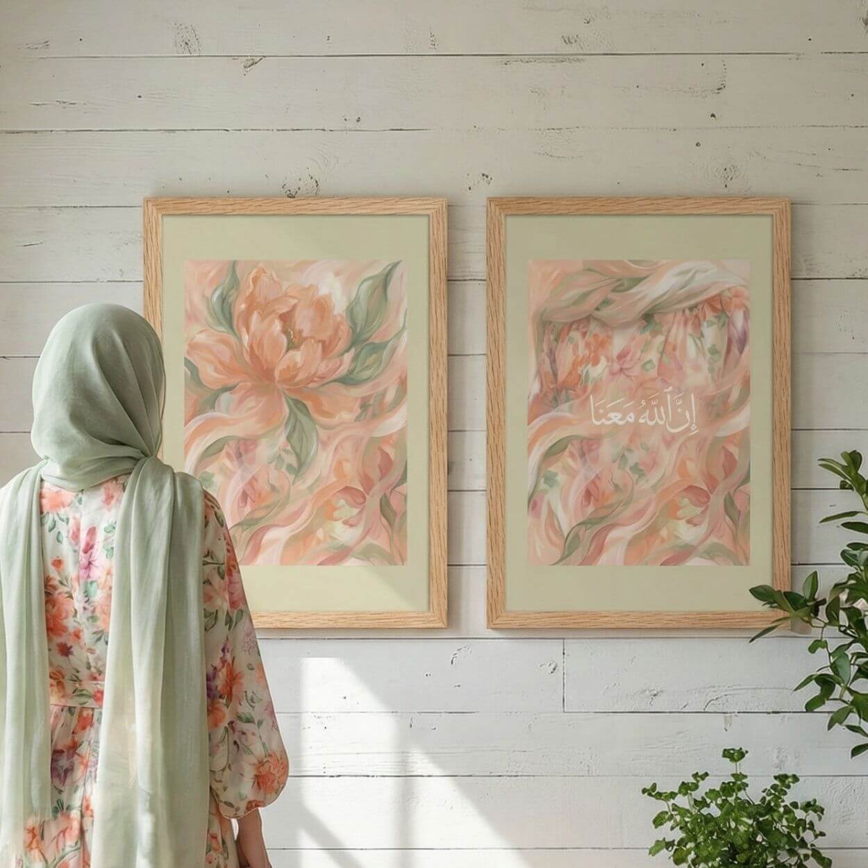 Woman in soft sage hijab viewing a pair of pastel Islamic wall art prints, including a floral printable and an Inna Allaha Ma’ana Arabic calligraphy print in natural wood frames